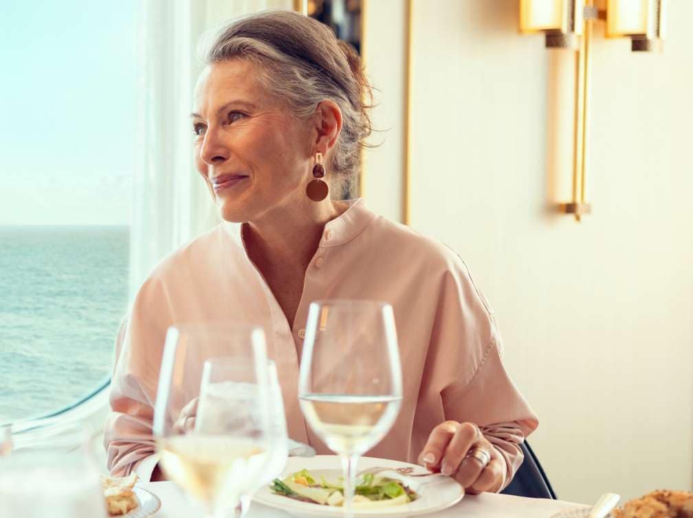 Guest dining in the elegant Britannia restaurant on a Cunard cruise ship with ocean views