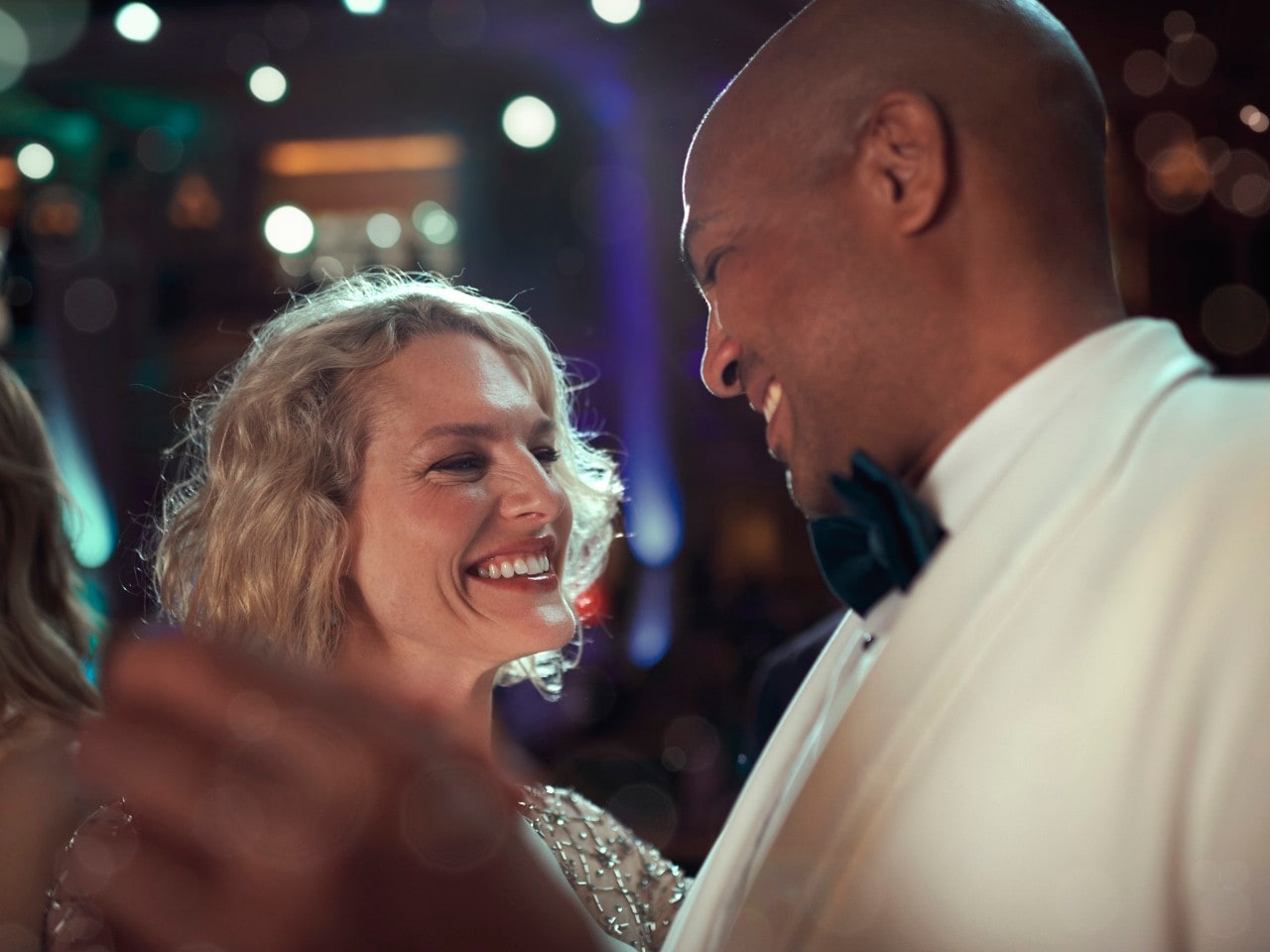 A man and a woman in formal dress sip champagne and look at one another on deck as the sun sets behind them