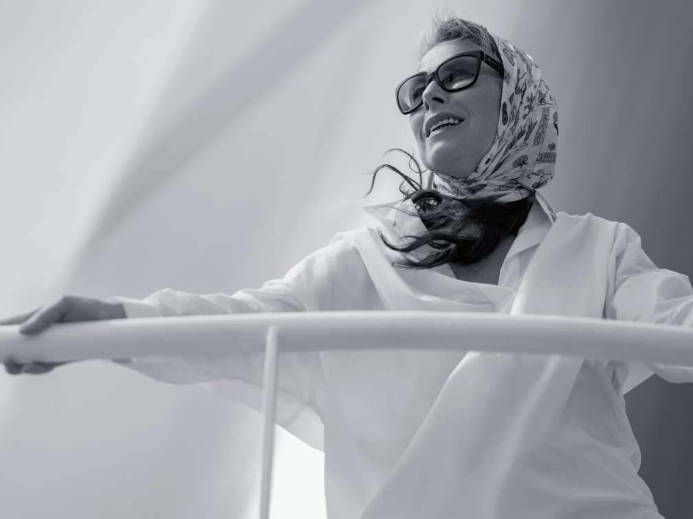 Person wearing sunglasses and a headscarf standing on a cruise ship deck in black and white