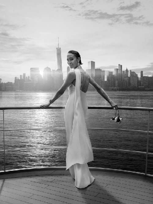 A woman stands on deck looking to camera, with New York city in the background