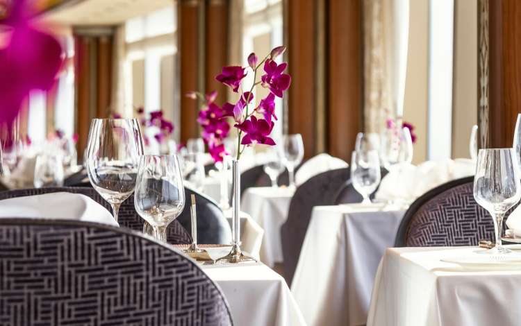 Queens Grill restaurant on Queen Elizabeth, showing seating, crockery and orchid decorations alongside seaview windows