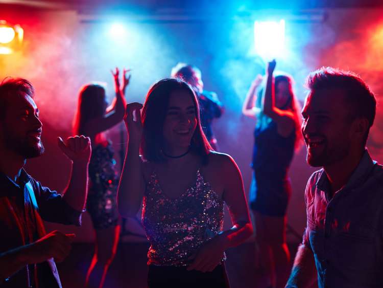 A group of smiling friends dance in a lit up nightclub