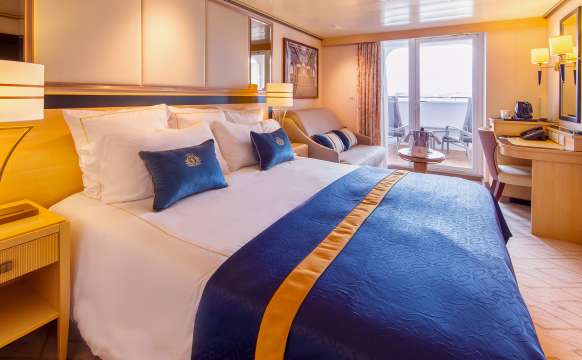 A typical sheltered balcony Britannia stateroom on Queen Mary 2, showing kingsize bed, living area and balcony access