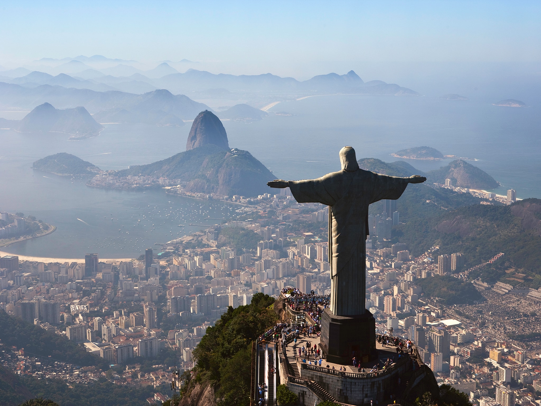 {"metadata_en_GB":{"alt-text":"A high-angle, rear-view shot of the iconic Christ the Redeemer statue standing atop Corcovado Mountain with arms outstretched, looking out over the sprawling urban landscape of Rio de Janeiro, Brazil. In the distance, Guanabara Bay, Sugarloaf Mountain, and layers of hazy mountain ridges stretch toward the horizon under a clear sky."},"metadata_de_DE":{"alt-text":"A high-angle, rear-view shot of the iconic Christ the Redeemer statue standing atop Corcovado Mountain with arms outstretched, looking out over the sprawling urban landscape of Rio de Janeiro, Brazil. In the distance, Guanabara Bay, Sugarloaf Mountain, and layers of hazy mountain ridges stretch toward the horizon under a clear sky."},"metadata_en_AU":{"alt-text":"A high-angle, rear-view shot of the iconic Christ the Redeemer statue standing atop Corcovado Mountain with arms outstretched, looking out over the sprawling urban landscape of Rio de Janeiro, Brazil. In the distance, Guanabara Bay, Sugarloaf Mountain, and layers of hazy mountain ridges stretch toward the horizon under a clear sky."},"metadata_en_US":{"alt-text":"A high-angle, rear-view shot of the iconic Christ the Redeemer statue standing atop Corcovado Mountain with arms outstretched, looking out over the sprawling urban landscape of Rio de Janeiro, Brazil. In the distance, Guanabara Bay, Sugarloaf Mountain, and layers of hazy mountain ridges stretch toward the horizon under a clear sky."}}