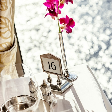 Table number, silverware and orchid on a table in the Queens Grill restaurant on Queen Elizabeth, with sparkling sea in the background