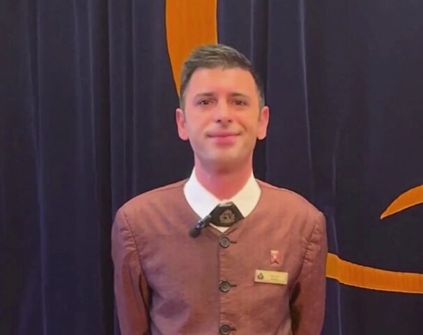 {"metadata_en_GB":{"alt-text":"A young man in uniform smiles in front of a blue velvet curtain"},"metadata_en_AU":{"alt-text":"A young man in uniform smiles in front of a blue velvet curtain"},"metadata_en_US":{"alt-text":"A young man in uniform smiles in front of a blue velvet curtain"}}