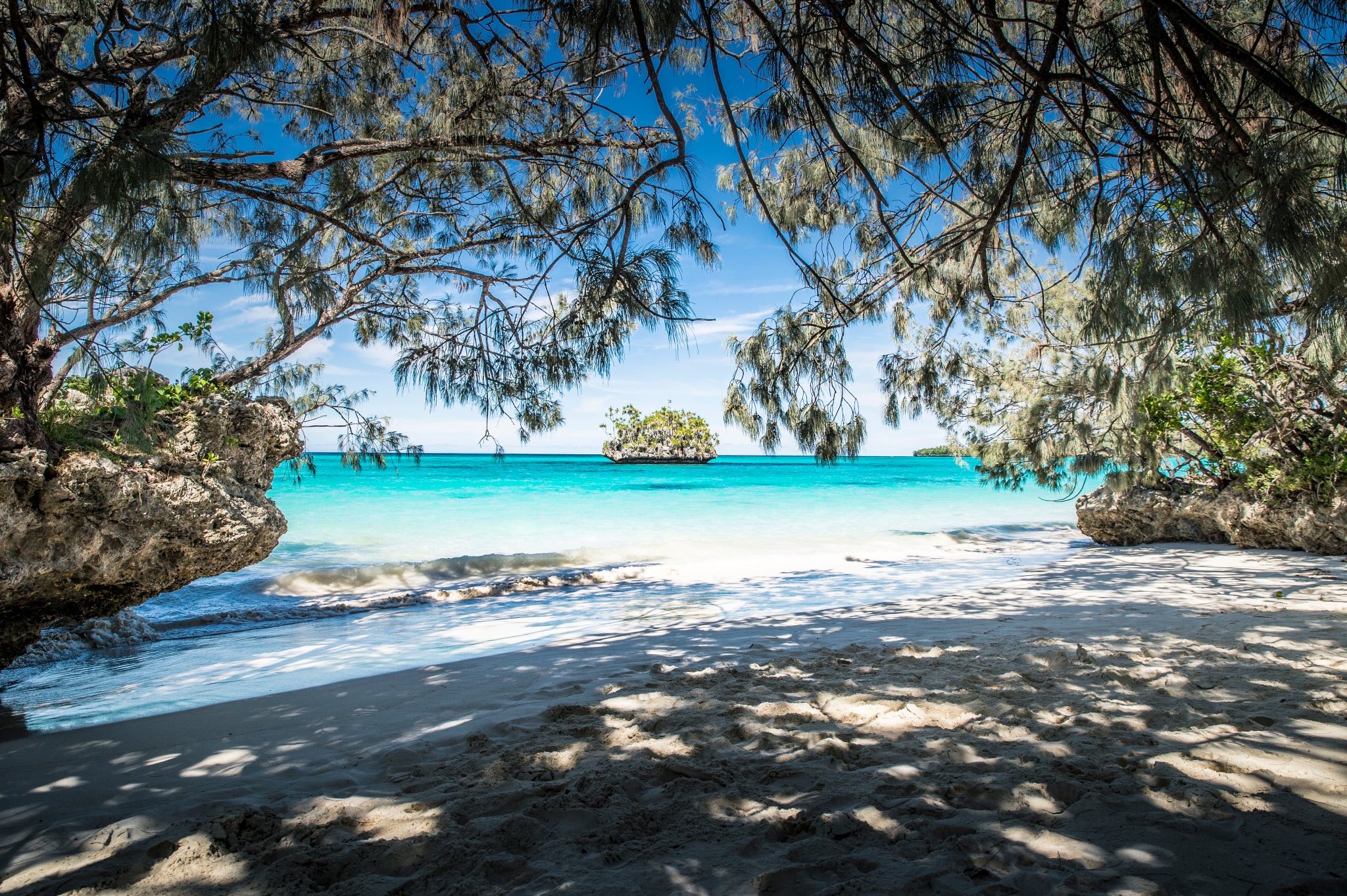 A beautiful view of Lifou beach, with trees causing a cool shadow over the sand.