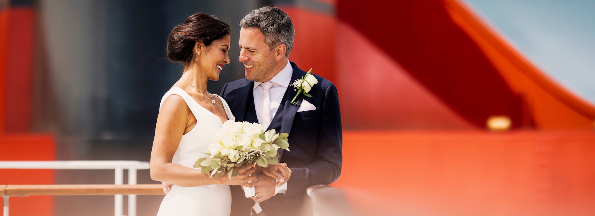 {"metadata_en_GB":{"alt-text":"A bride and groom hold a bouquet of flowers in front of the red funnel of a Cunard cruise ship"},"metadata_de_DE":{"alt-text":"Eine Braut und ein Bräutigam halten einen Blumenstrauß vor dem roten Schornstein eines Cunard-Kreuzfahrtschiffs"},"metadata_en_AU":{"alt-text":"A bride and groom hold a bouquet of flowers in front of the red funnel of a Cunard cruise ship"},"metadata_en_US":{"alt-text":"A bride and groom hold a bouquet of flowers in front of the red funnel of a Cunard cruise ship"}}